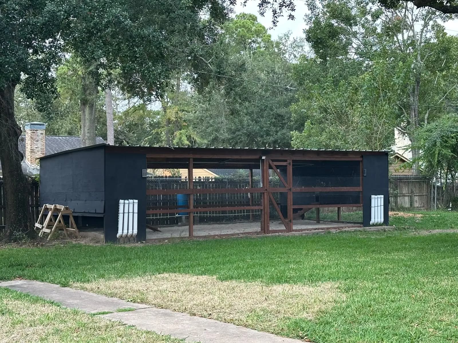 A newly built wooden chicken coop with a metal roof and open wire bays, on a grassy yard.
